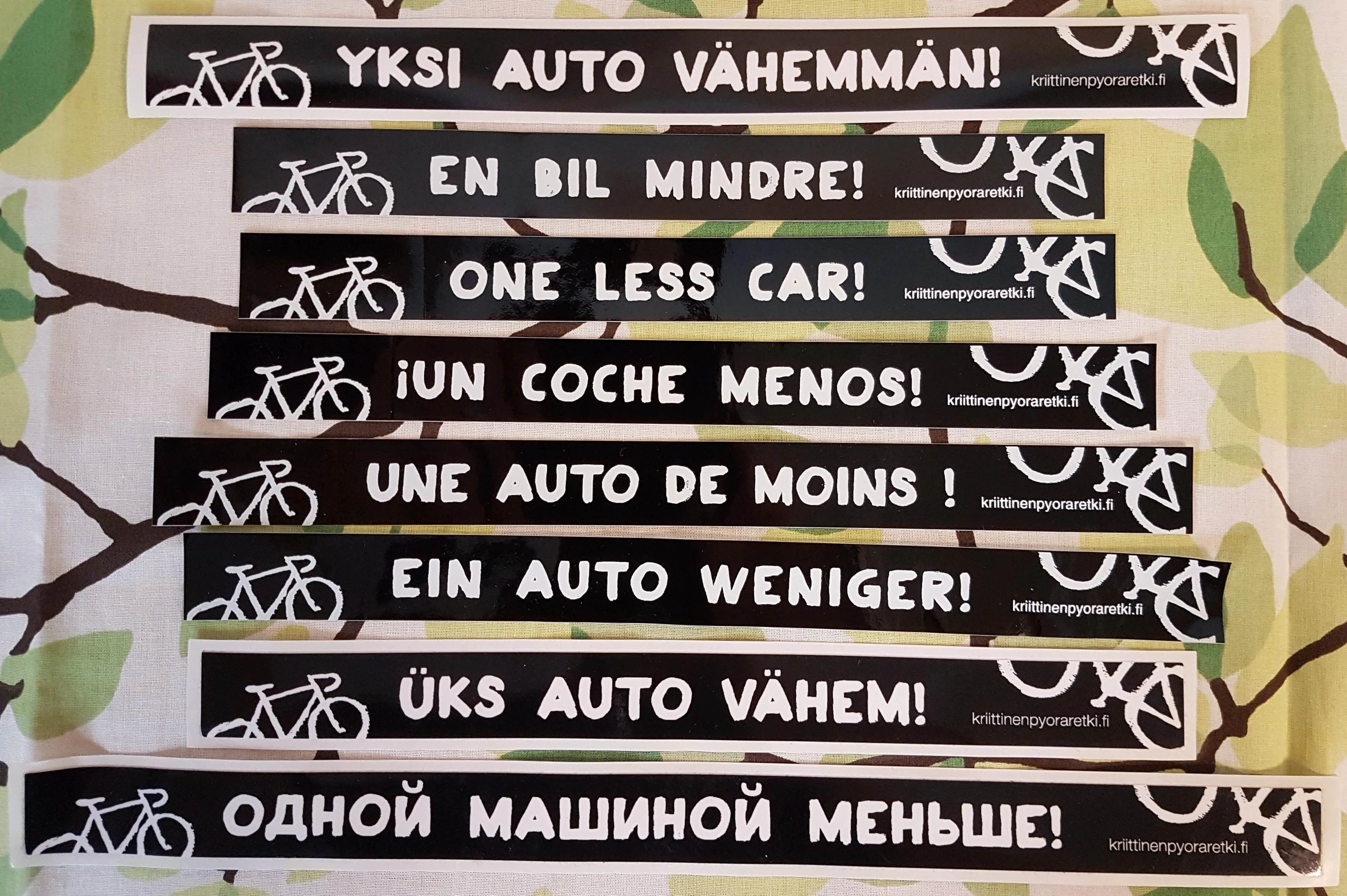 Yksi auto vähemmän -tarra on saatavilla kahdeksalla eri kielellä.